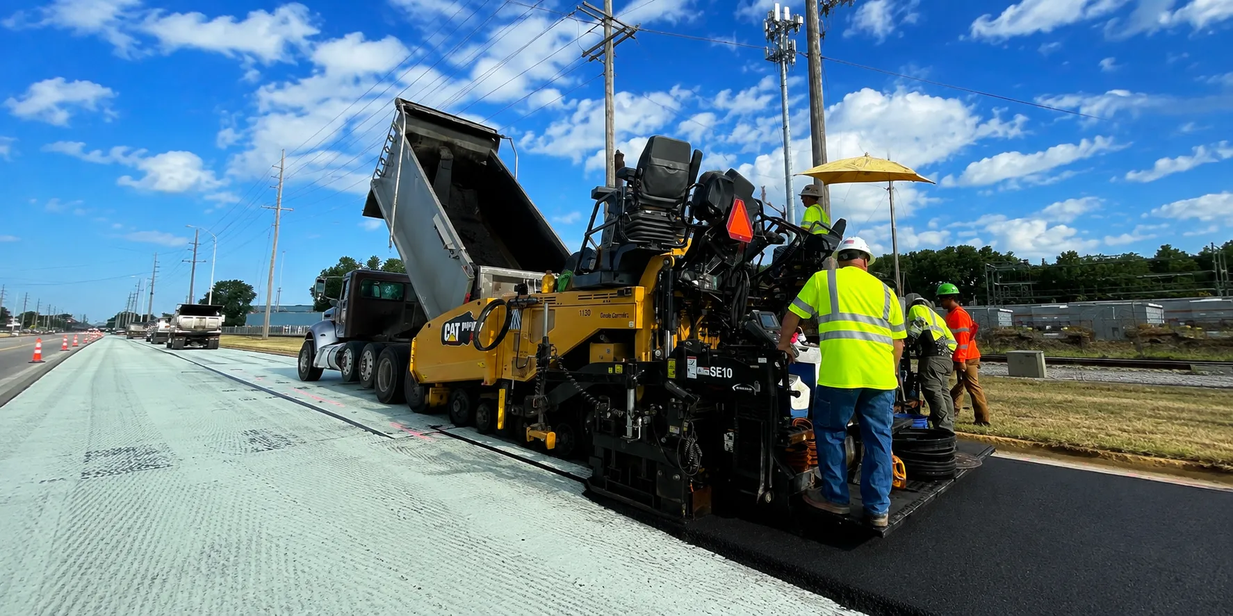 Paver laying new asphalt over a paving fabric interlayer as a dump truck feeds the hopper
