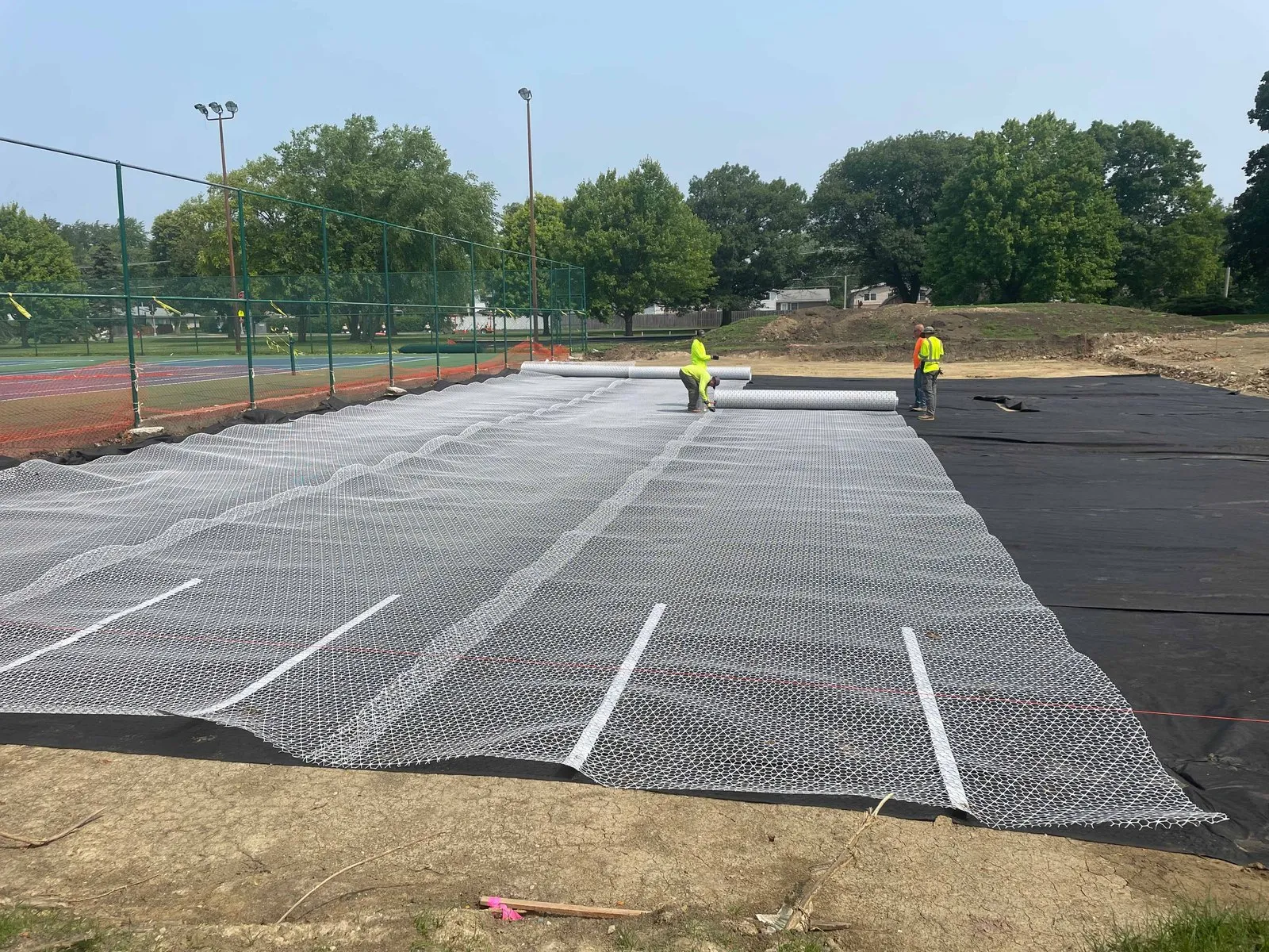 Crew rolling out geogrid over geotextile at a tennis court reconstruction