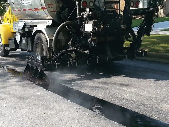 Spray truck applying crack sealant bands on a neighborhood street