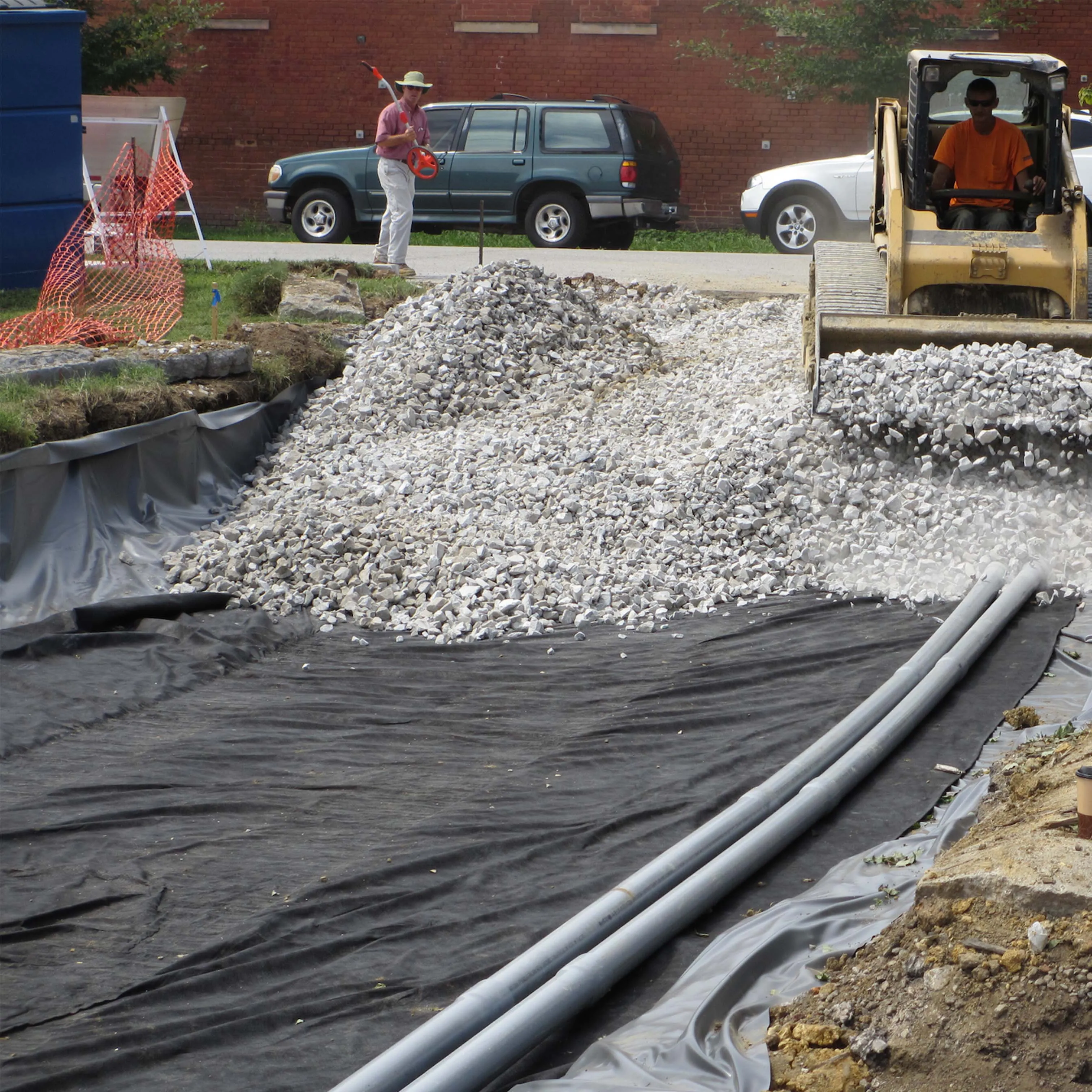 Nonwoven geotextile being covered with stone over drainage pipes